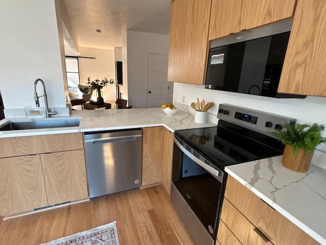 kitchen with stainless steel appliances, light brown cabinets, a sink, modern cabinets, and light wood-type flooring