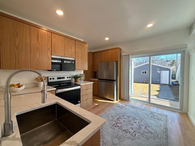 kitchen with appliances with stainless steel finishes, recessed lighting, light wood-style flooring, and light stone countertops