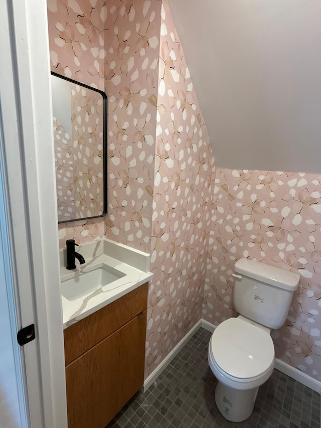 bathroom featuring toilet, vanity, tile patterned flooring, baseboards, and wallpapered walls