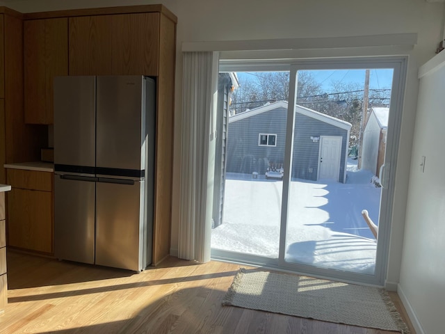 kitchen with brown cabinetry, light wood-type flooring, freestanding refrigerator, and baseboards