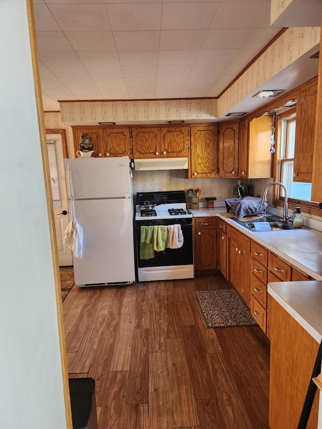 kitchen with gas stove, freestanding refrigerator, under cabinet range hood, brown cabinets, and a sink