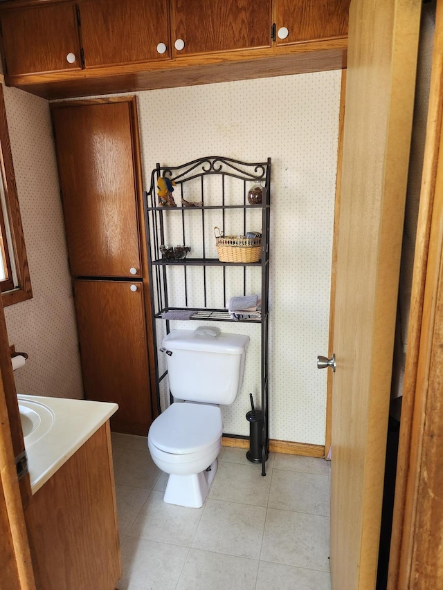 half bathroom with toilet, tile patterned floors, wallpapered walls, and vanity