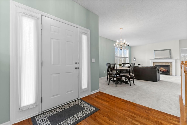 entrance foyer with a tiled fireplace, a textured ceiling, wood finished floors, a chandelier, and baseboards