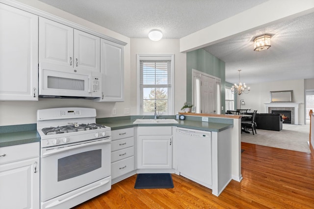 kitchen featuring a warm lit fireplace, a peninsula, white appliances, a sink, and dark countertops