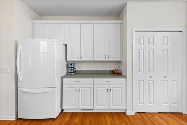 kitchen with baseboards, white cabinetry, wood finished floors, and freestanding refrigerator