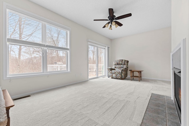 living area featuring a textured ceiling, carpet floors, a fireplace with flush hearth, visible vents, and baseboards