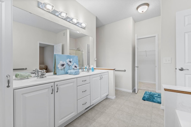 bathroom featuring double vanity, a stall shower, a spacious closet, a textured ceiling, and a sink