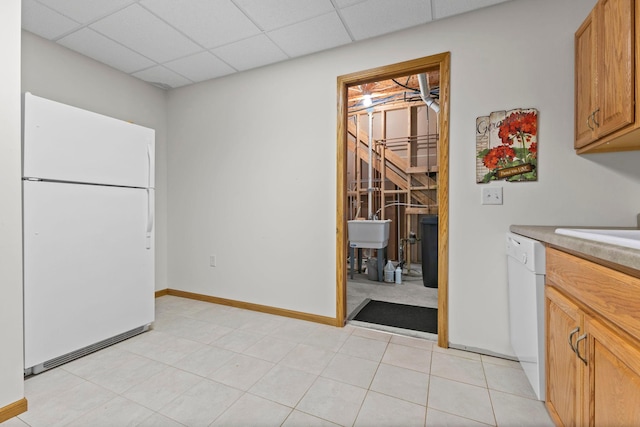 interior space featuring a drop ceiling, a sink, baseboards, and light tile patterned floors