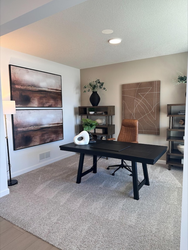 carpeted office featuring a textured ceiling, visible vents, and baseboards