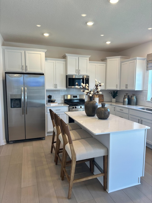 kitchen featuring stainless steel appliances, backsplash, white cabinetry, a kitchen island, and a sink