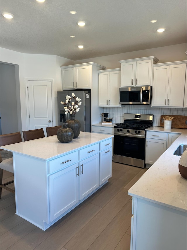 kitchen featuring stainless steel appliances, a breakfast bar, wood finished floors, white cabinets, and tasteful backsplash