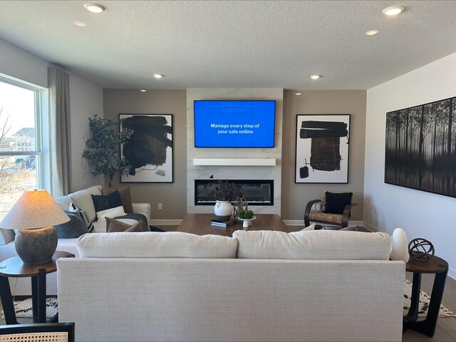 living room featuring a glass covered fireplace, a textured ceiling, baseboards, and wood finished floors