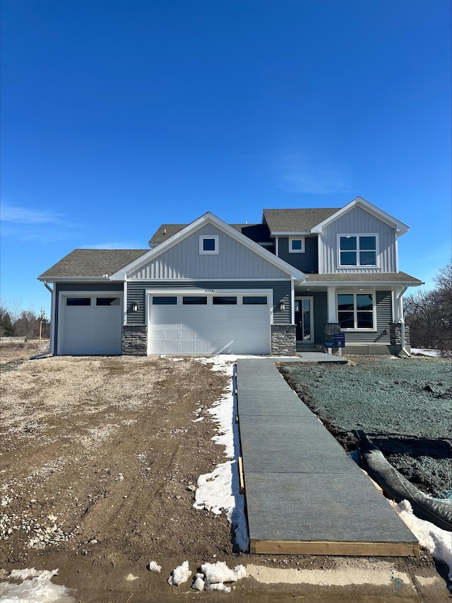 view of front of property with a garage, driveway, stone siding, roof with shingles, and board and batten siding