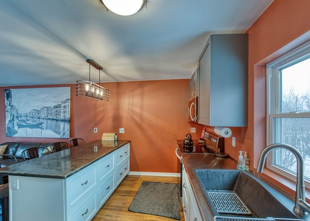 kitchen featuring a peninsula, range with electric cooktop, a sink, light wood-style floors, and stainless steel microwave