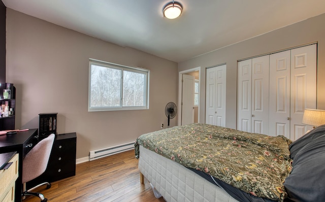 bedroom with a baseboard radiator, wood finished floors, two closets, and baseboards