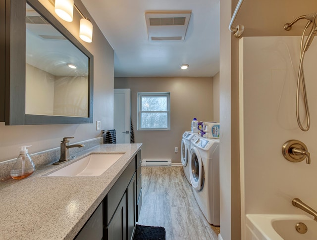 laundry area with laundry area, washing machine and clothes dryer, baseboard heating, light wood-type flooring, and a sink