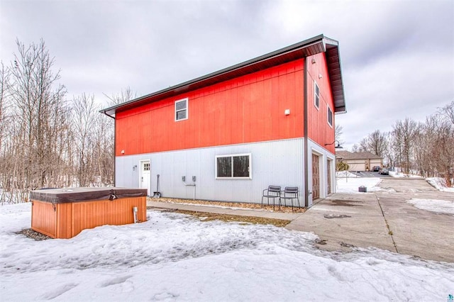 snow covered rear of property with a hot tub