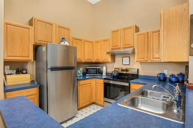 kitchen featuring under cabinet range hood, a high ceiling, a sink, appliances with stainless steel finishes, and dark countertops