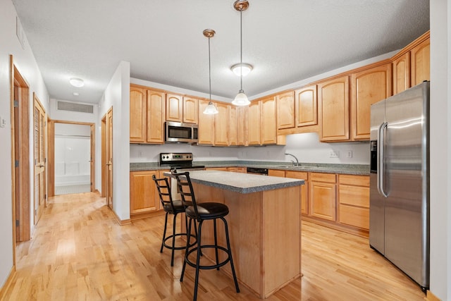 kitchen with visible vents, a kitchen island, stainless steel appliances, light wood-style floors, and dark countertops