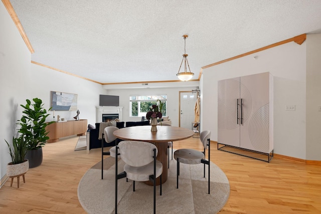 dining area with crown molding, light wood-type flooring, a warm lit fireplace, and a textured ceiling