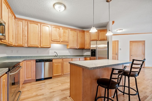 kitchen featuring light wood finished floors, a breakfast bar, a sink, appliances with stainless steel finishes, and a textured ceiling