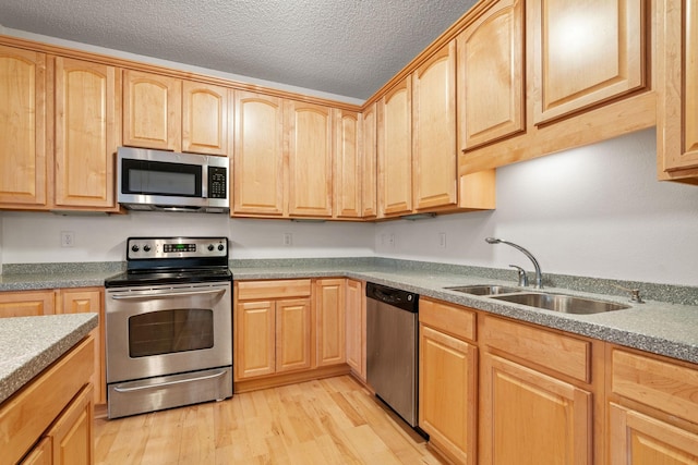 kitchen with light brown cabinetry, a sink, a textured ceiling, stainless steel appliances, and light wood finished floors