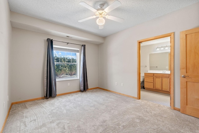 unfurnished bedroom featuring light carpet, connected bathroom, a textured ceiling, and baseboards