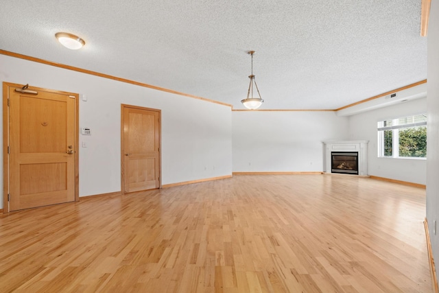 unfurnished living room with a glass covered fireplace, crown molding, light wood finished floors, and a textured ceiling