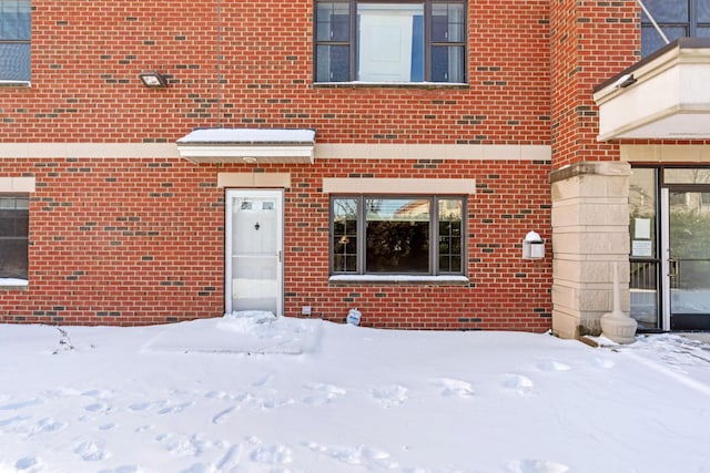 snow covered property entrance featuring brick siding