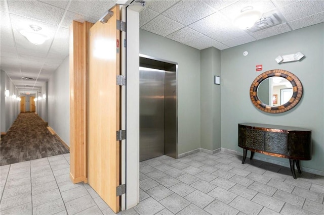 hall with elevator, a drop ceiling, baseboards, and light tile patterned floors