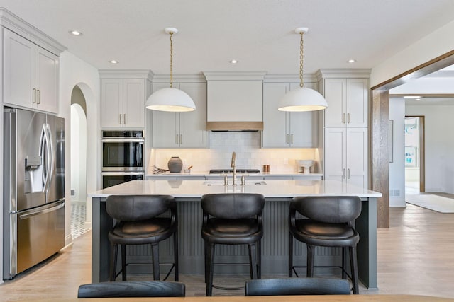 kitchen with decorative backsplash, light wood-style flooring, stainless steel appliances, light countertops, and premium range hood