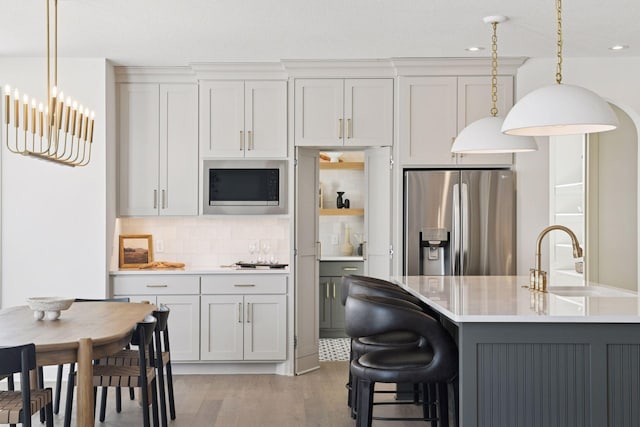 kitchen featuring light countertops, backsplash, a sink, built in microwave, and stainless steel fridge with ice dispenser