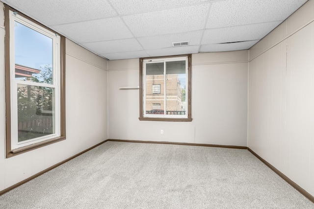 carpeted spare room featuring baseboards, visible vents, and a drop ceiling