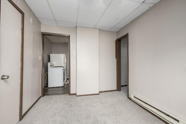 empty room featuring a paneled ceiling, baseboards, baseboard heating, carpet, and washer / dryer