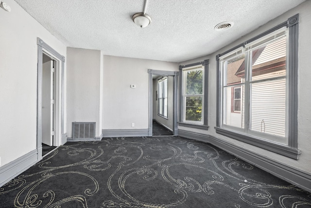 unfurnished room with visible vents, dark carpet, a textured ceiling, and baseboards