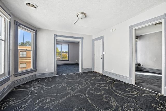 unfurnished room with baseboards, visible vents, dark colored carpet, and a textured ceiling