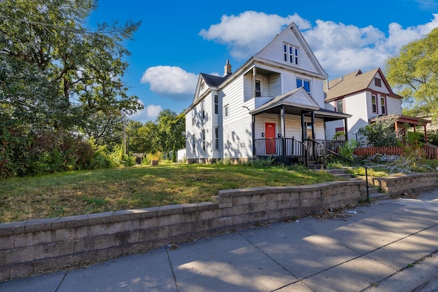 view of front facade with covered porch, a front lawn, and a chimney