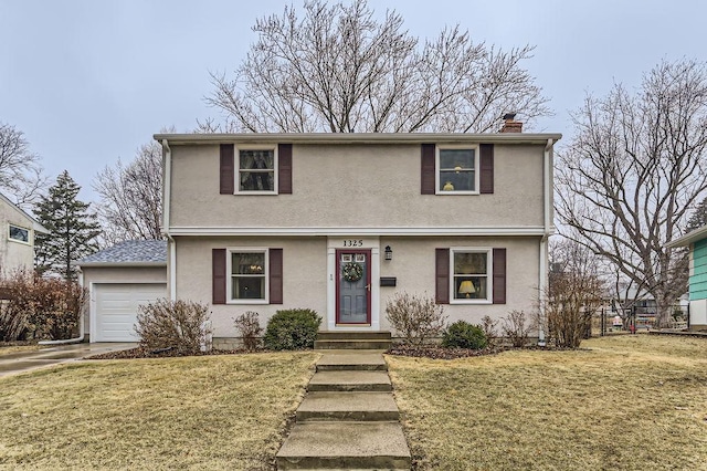 colonial house featuring an attached garage, a chimney, a front lawn, and stucco siding