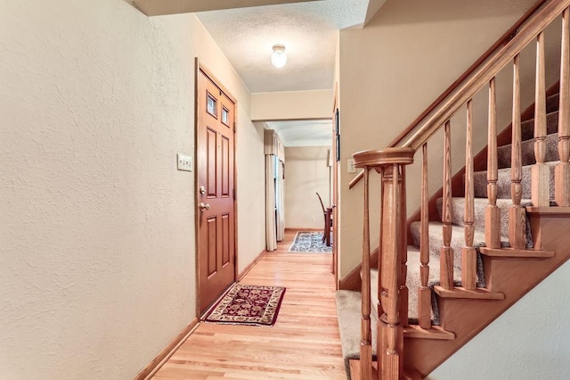 interior space featuring a textured wall, light wood-style flooring, a textured ceiling, and stairs