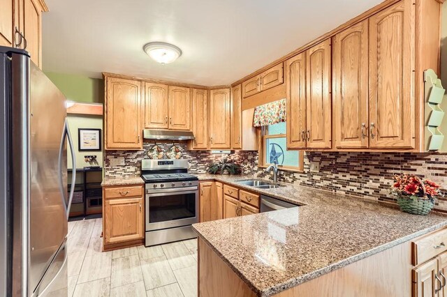 kitchen with light stone counters, under cabinet range hood, stainless steel appliances, a sink, and decorative backsplash