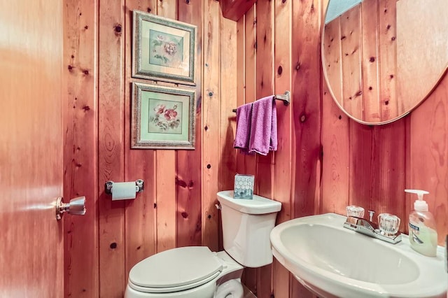 bathroom with a sink, toilet, and wooden walls