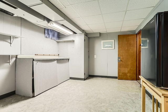 finished below grade area with black refrigerator, baseboards, a paneled ceiling, and light floors