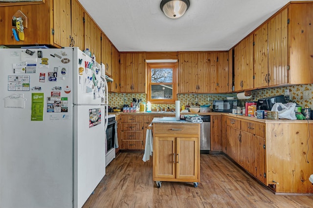 kitchen featuring black microwave, light countertops, decorative backsplash, freestanding refrigerator, and stove