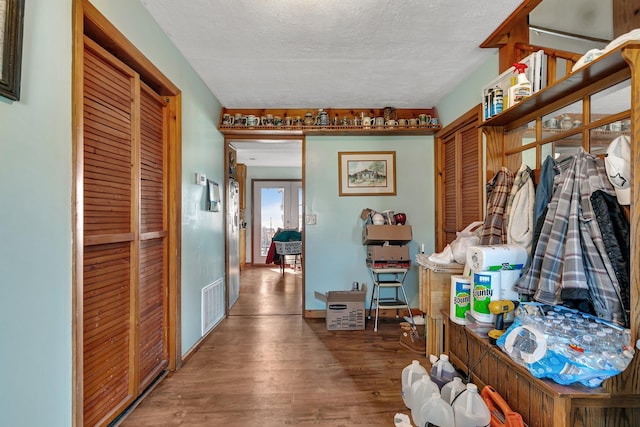 hall with baseboards, wood finished floors, visible vents, and a textured ceiling