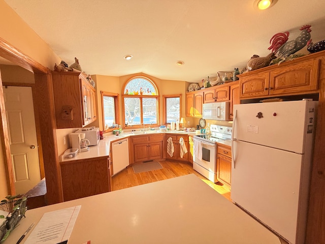 kitchen featuring brown cabinets, light countertops, light wood-style floors, vaulted ceiling, and white appliances