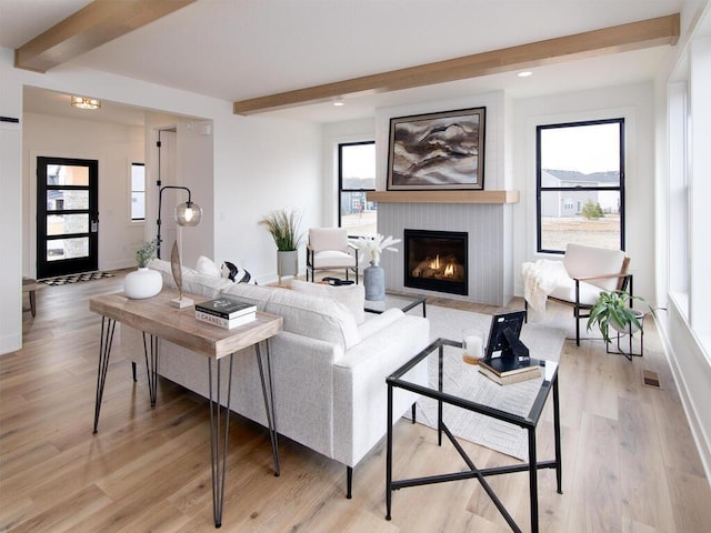 living room featuring baseboards, beamed ceiling, a lit fireplace, and light wood finished floors