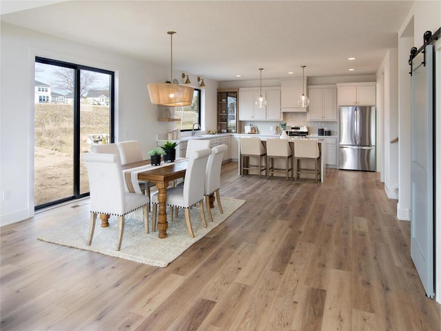 dining room featuring a barn door, light wood-style flooring, and recessed lighting