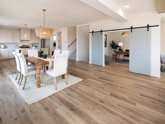 dining area featuring a barn door, light wood-style flooring, recessed lighting, stairway, and beam ceiling