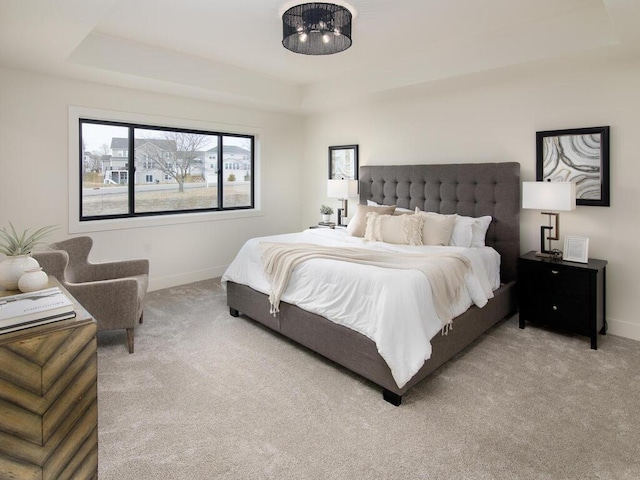 carpeted bedroom with baseboards and a raised ceiling