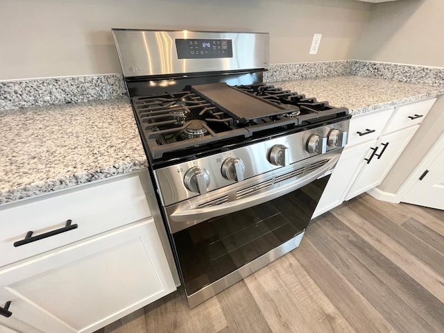 kitchen featuring light wood finished floors, gas stove, light stone countertops, and white cabinets